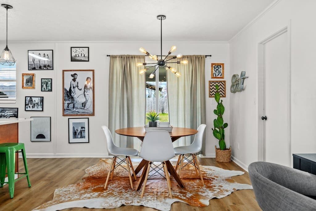 A dining area with a round table, white chairs, a cowhide rug, and a hanging light fixture.