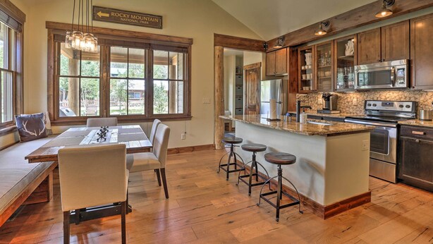 A spacious kitchen with wooden cabinets, a large island with stools, and a view of Rocky Mountain National Park. - Walk to Main St & Marina: Grand Lake Cabin! (Grand Lake)