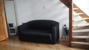 Une pièce avec un canapé de couleur sombre, un escalier en bois et une petite table avec une lampe.