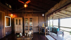 A wooden interior with a ceiling fan, a wooden cabinet with glass doors, a table with a decorative horse figurine, and a bench on an outdoor deck.