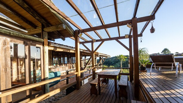 A wooden deck with a glass ceiling, wooden benches, and a table.