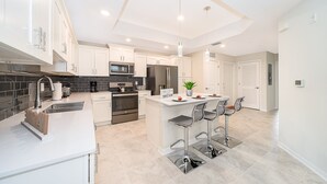 Una cocina moderna con armarios blancos, electrodomésticos de acero inoxidable y una isla central con taburetes de bar.