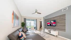 Una sala moderna con un sofá modular, un televisor de pantalla plana montado en una pared de madera y un ventilador de techo.