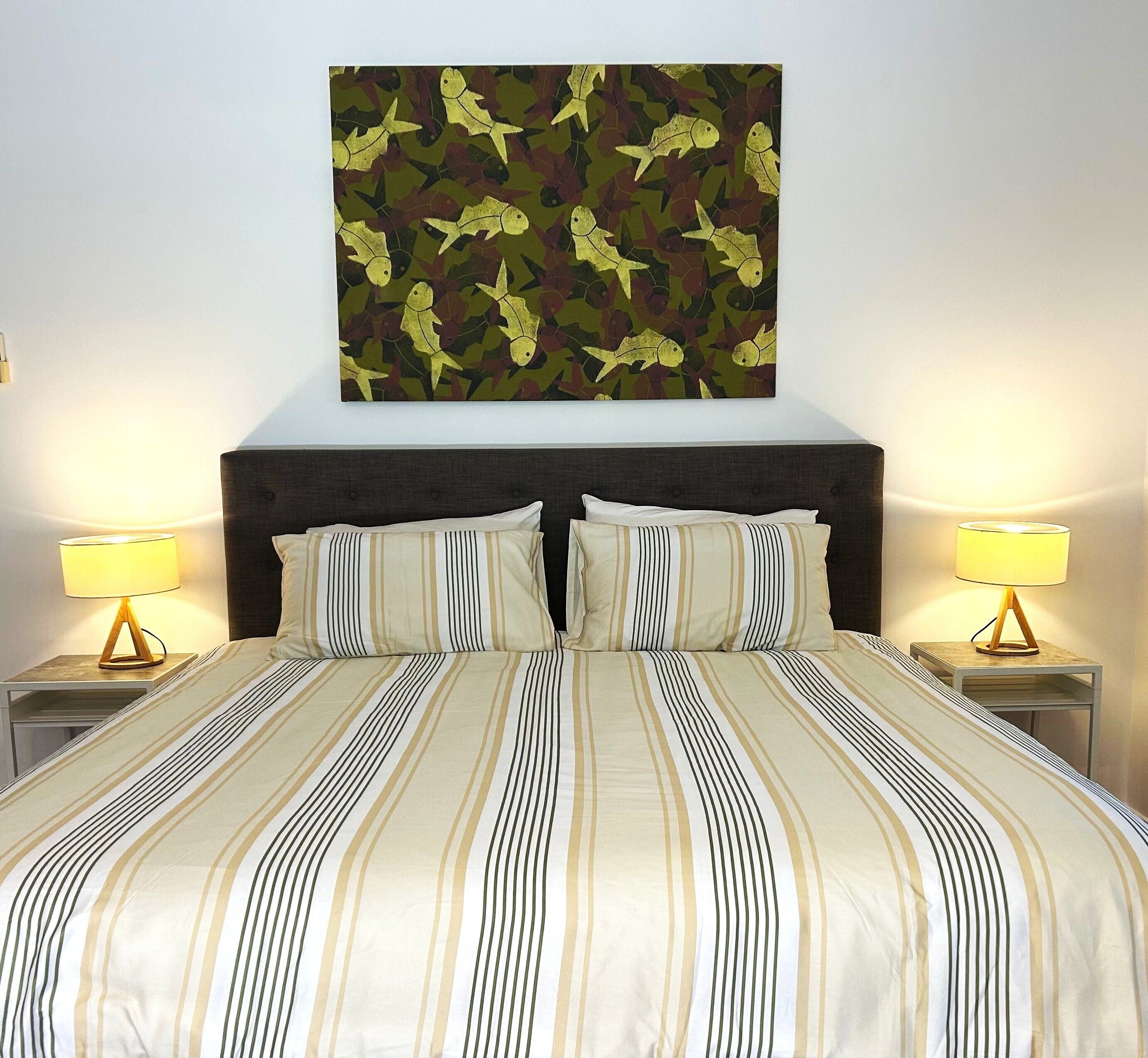 Een hotelkamer met een groot bed, twee nachtkastjes met lampen en een kunstwerk aan de muur.