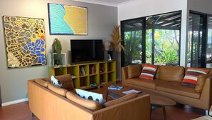 A living room with a sofa, a coffee table, a TV, and a bookshelf. - Cable Beach Haven - 3BR house with pool, 5 minutes walk to Cable Beach  (Cable Beach)