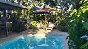 A swimming pool with lounge chairs and an umbrella, surrounded by lush greenery. - Cable Beach Haven - 3BR house with pool, 5 minutes walk to Cable Beach  (Cable Beach)