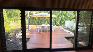 A patio area with a table and chairs, an umbrella, and a view of a garden through a glass door. - Cable Beach Haven - 3BR house with pool, 5 minutes walk to Cable Beach  (Cable Beach)