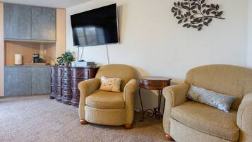 A living room with two armchairs, a coffee table, a flat-screen TV, a decorative metal piece, and a wooden cabinet with drawers.
