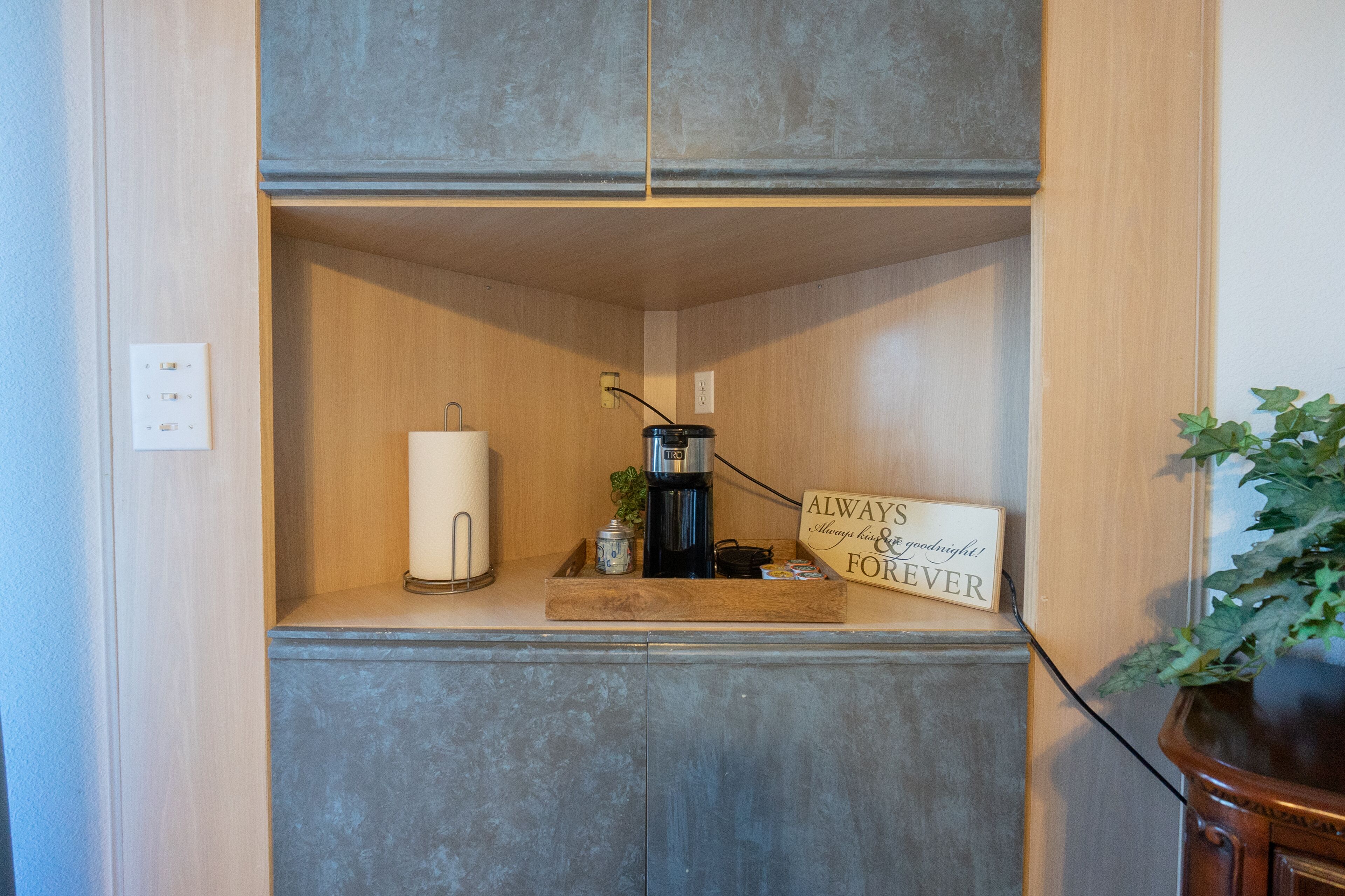 A small kitchenette with a coffee maker, a roll of paper towels, and a sign that says "Always Goodnight & Forever".