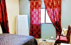 Um quarto com uma cama, uma cadeira, uma janela com cortinas e um radiador.