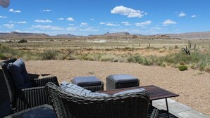 A patio with wicker furniture and a table, overlooking a desert landscape with sparse vegetation and distant hills. - Little Ranch Home near National Parks & Lake Powell (Clark Bench)