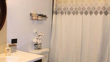 A bathroom with a white toilet, a wooden vanity, a shower curtain with a geometric pattern, and a small shelf with toiletries.