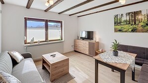 Moderni olohuone, jossa on sohva, sohvapöytä, televisio ja ruokapöytä.