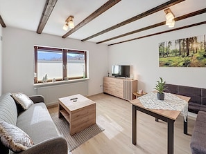 A modern living room with a sofa, coffee table, TV, and a dining table. - Franzi 1 by Interhome (Arrach)
