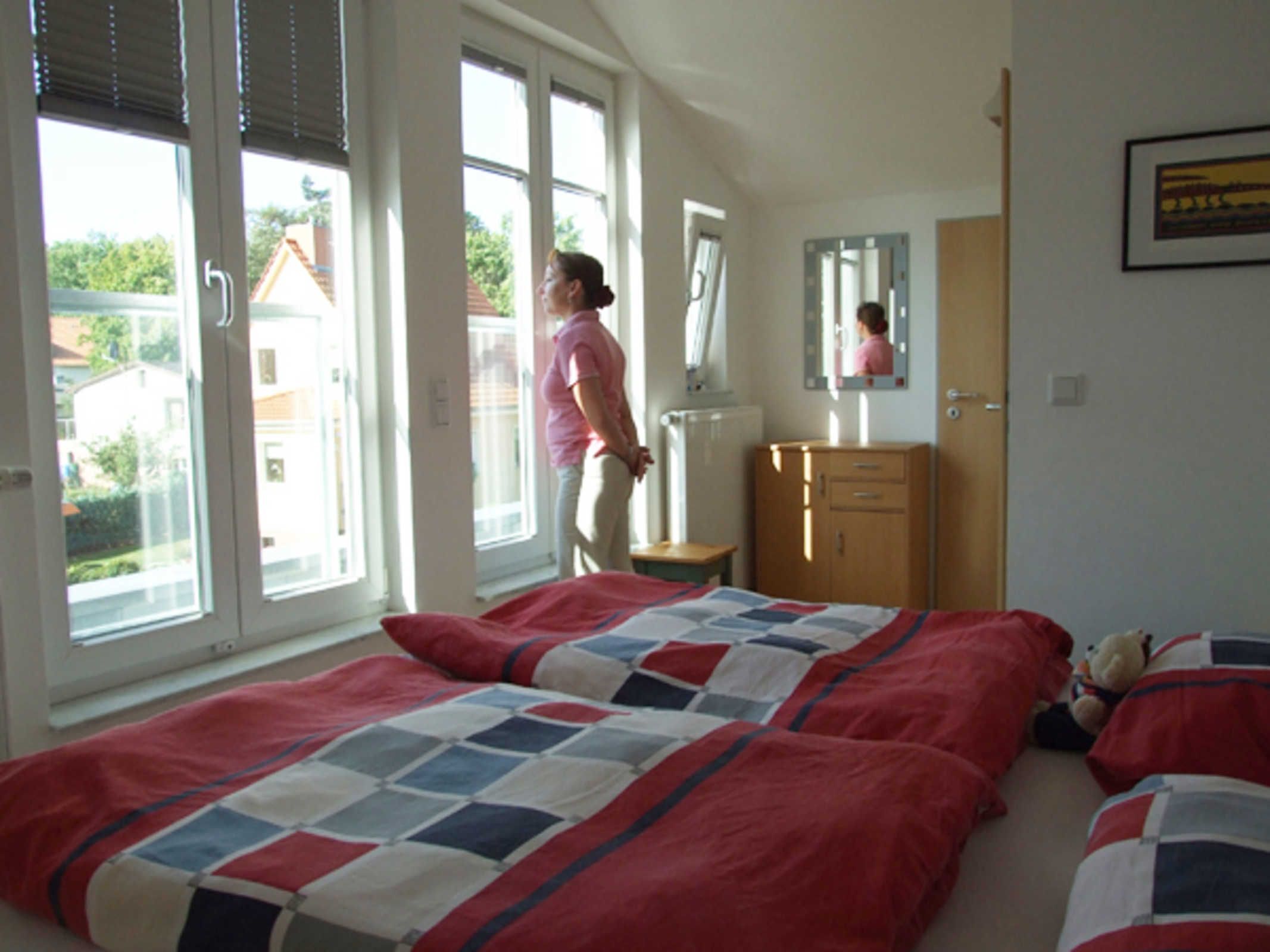 Ein Schlafzimmer mit zwei Betten, einer Holzkommode, einem Spiegel und einem Fenster mit Jalousien.