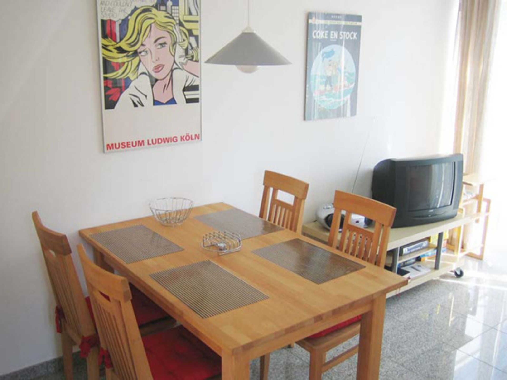 A dining area with a wooden table, chairs, and a television on a stand.