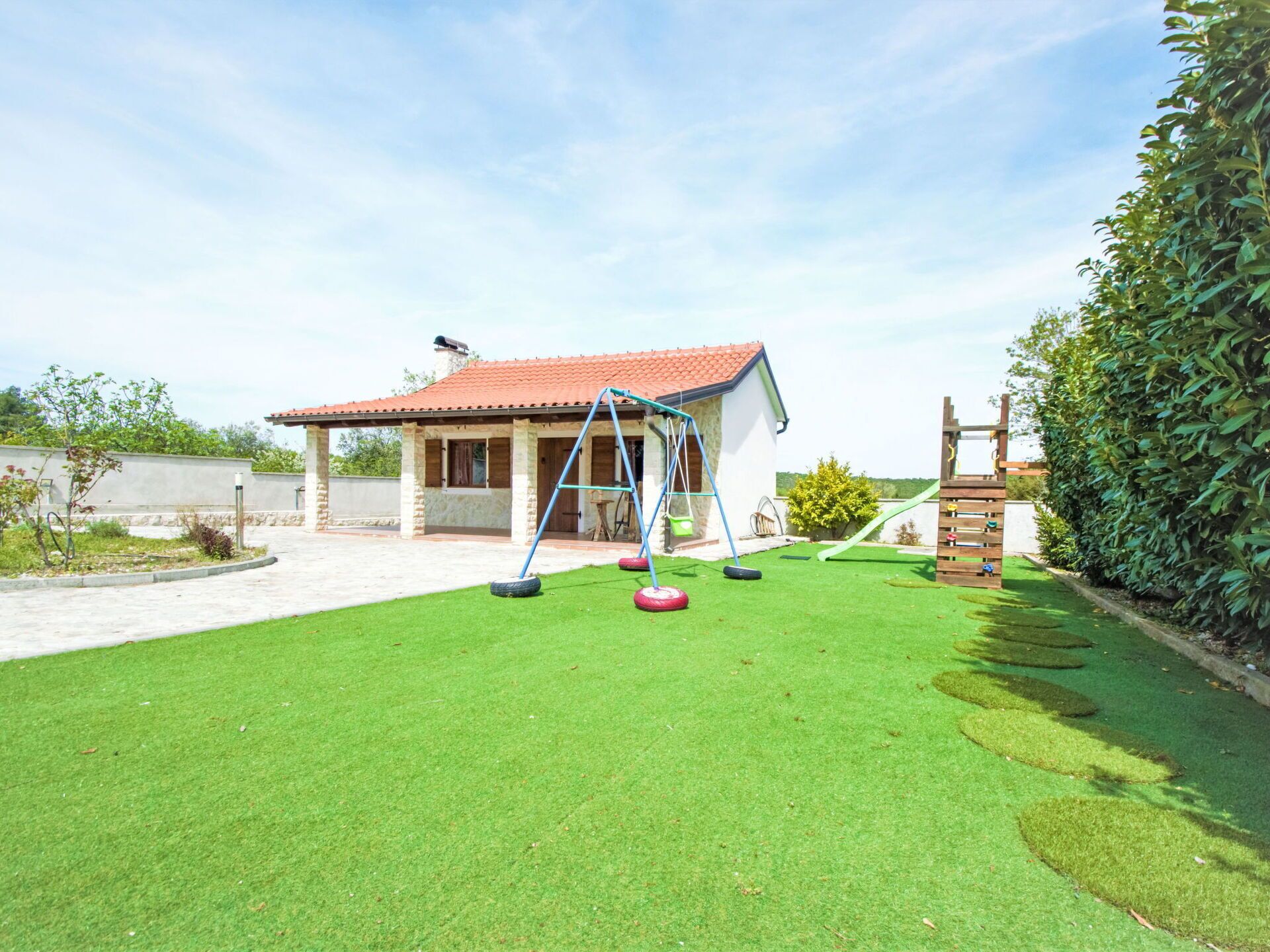 A house with a red-tiled roof, a swing set, and a slide in a well-maintained backyard.