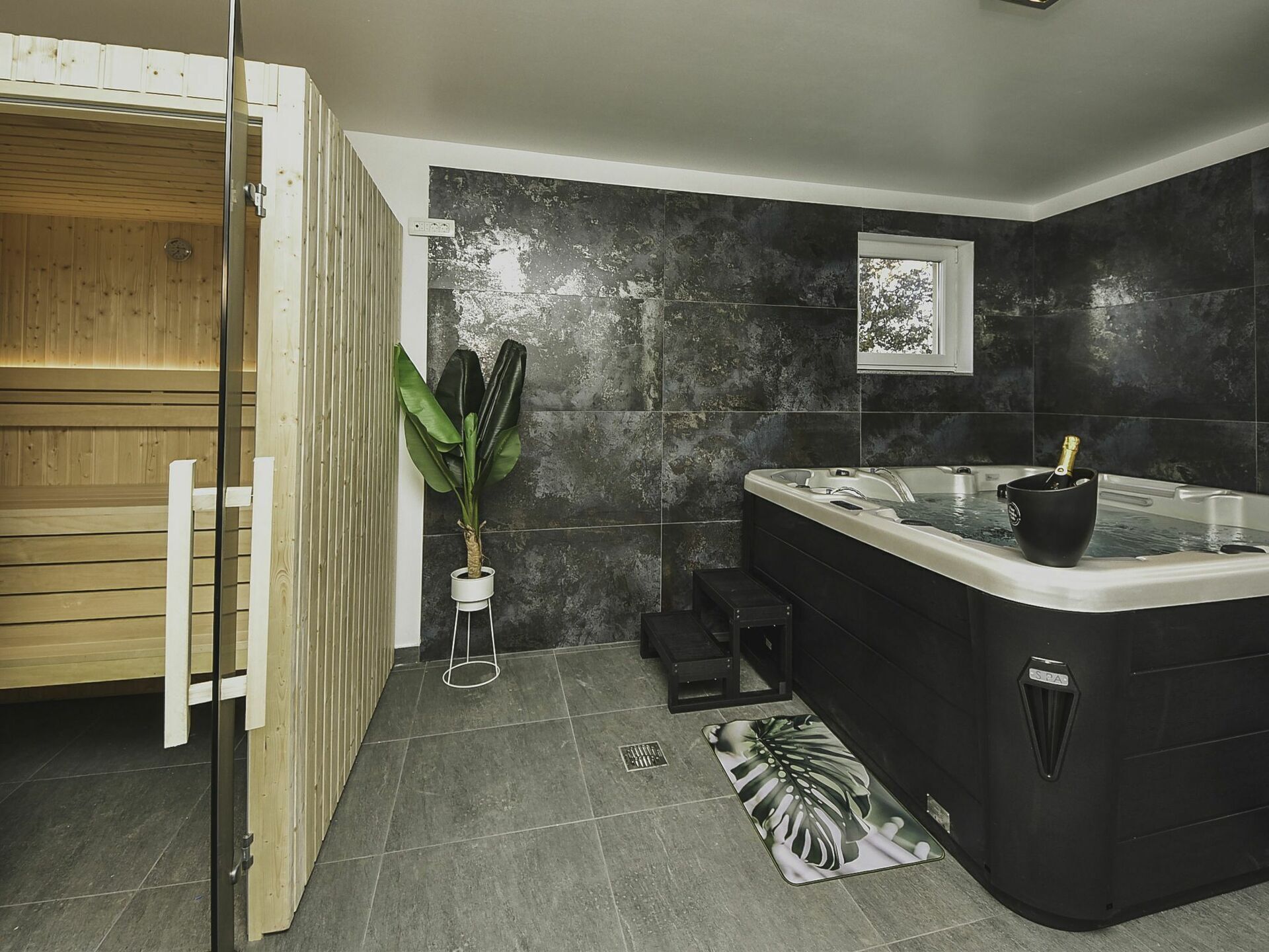 Ein modernes Badezimmer mit Sauna, einer großen schwarzen Badewanne und einer Topfpflanze.