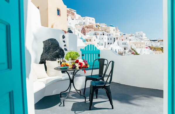 A terrace with a white sofa, a black chair, and a table with flowers and fruits.