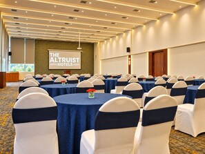 Uma sala de conferências no The Altruist Hotels, com mesas redondas, cadeiras e uma tela de projetor.