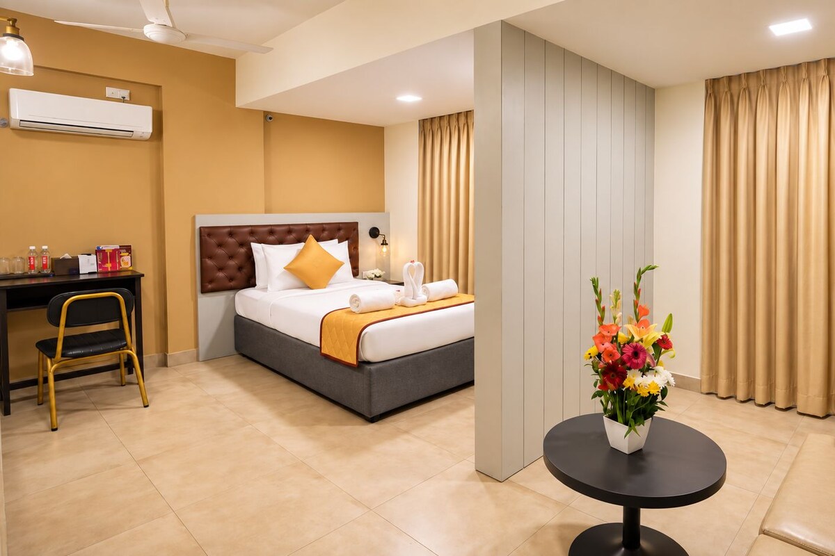 A hotel room with a bed, a desk, a chair, a coffee table, and a vase of flowers.