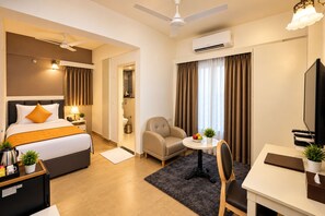 A hotel room with a bed, a desk, a chair, a small table with a plant, and an air conditioning unit. - The Altruist Whitefield Hotel (Bengaluru)