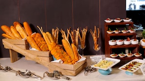 A buffet table with various food items including baguettes, small bowls of appetizers, and a sign indicating a creamy lemon couscous salad. - The Altruist Whitefield Hotel (Bengaluru)