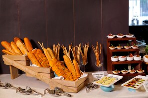 A buffet table with various food items including baguettes, small bowls of appetizers, and a sign indicating a creamy lemon couscous salad. - The Altruist Whitefield Hotel (Bengaluru)