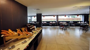 A spacious dining area with multiple tables and chairs, a buffet line with various food items, and large windows providing natural light. - The Altruist Whitefield Hotel (Bengaluru)