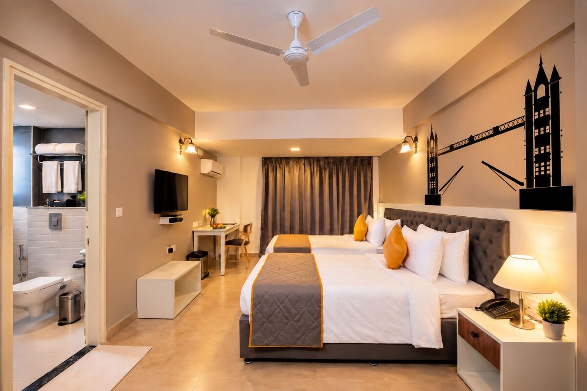 A hotel room with a bed, bedside table, TV, desk, chair, and a bathroom visible through an open door.
