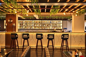 A bar area with a marble countertop, bar stools, and a variety of bottles and glasses. - The Altruist Whitefield Hotel (Bengaluru)