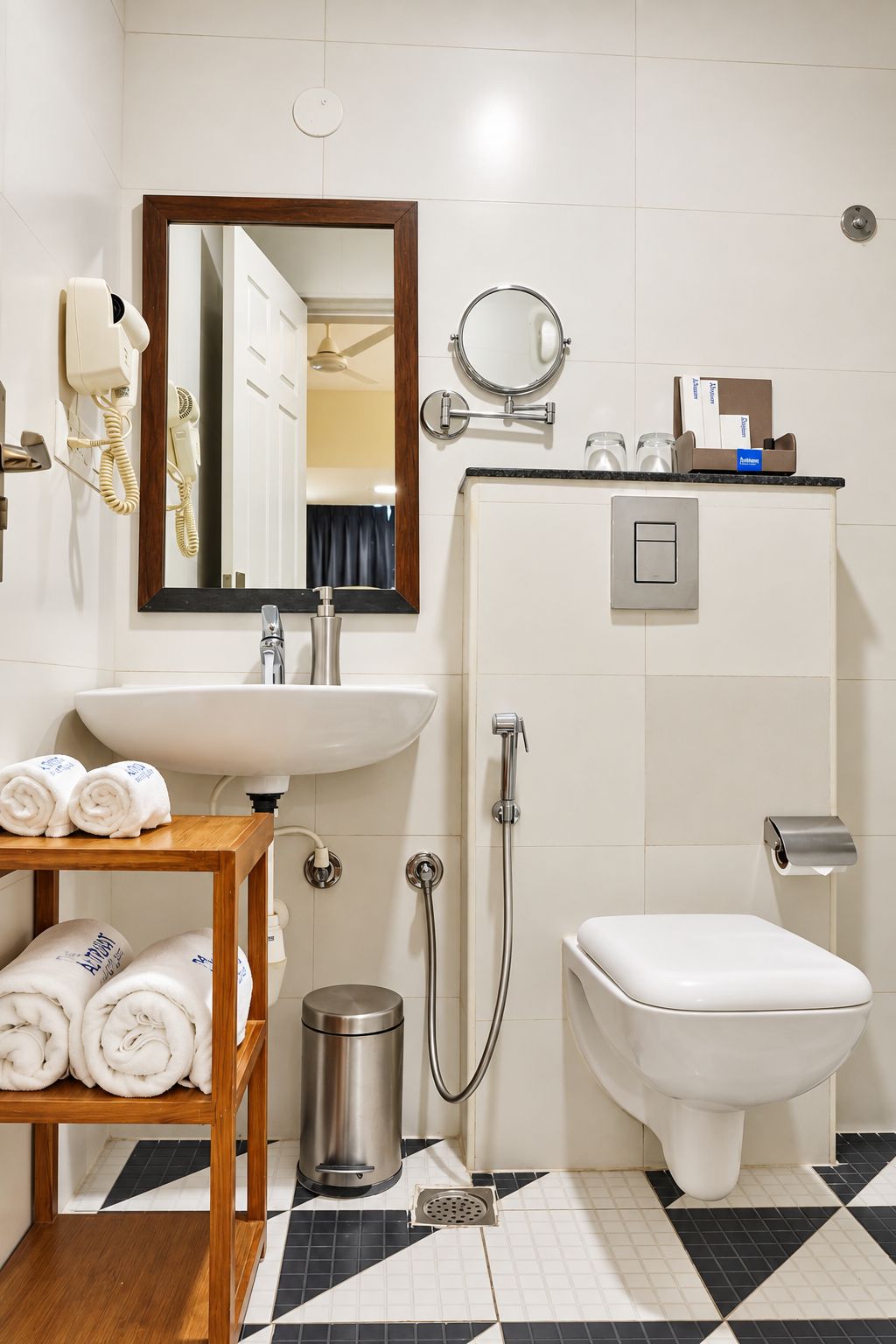 A bathroom with a sink, mirror, towel rack, toilet, shower, and a waste bin.