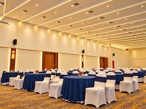 A conference room with rows of tables and chairs, equipped with ceiling lights and a projector.