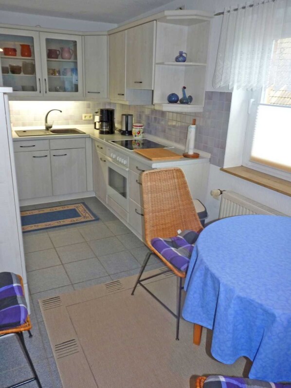 A compact kitchen with white cabinets, a sink, a stove, and a dining area with a table and chairs.