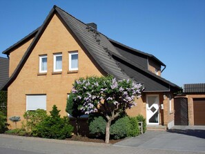 A two-story brick house with a sloped roof, a front garage door, and a small tree with purple flowers.