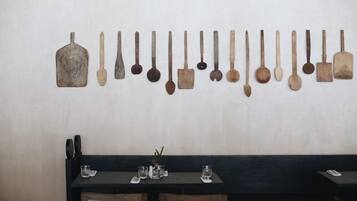 Un comedor con una mesa larga y sillas, un expositor empotrado en la pared con diversos utensilios, y una decoración sencilla en la pared.