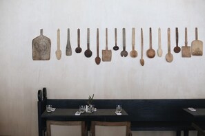 Un comedor con una mesa larga y sillas, un expositor empotrado en la pared con diversos utensilios, y una decoración sencilla en la pared.