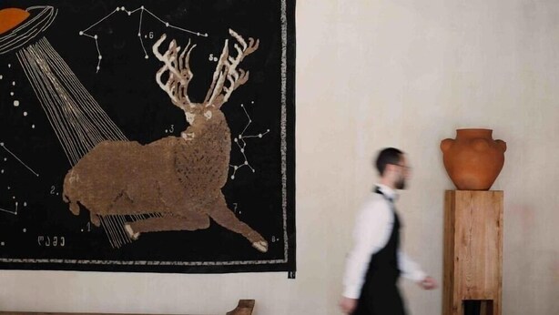 Une personne qui passe devant un mur orné d’une grande illustration représentant un cerf, avec un banc en bois à proximité.