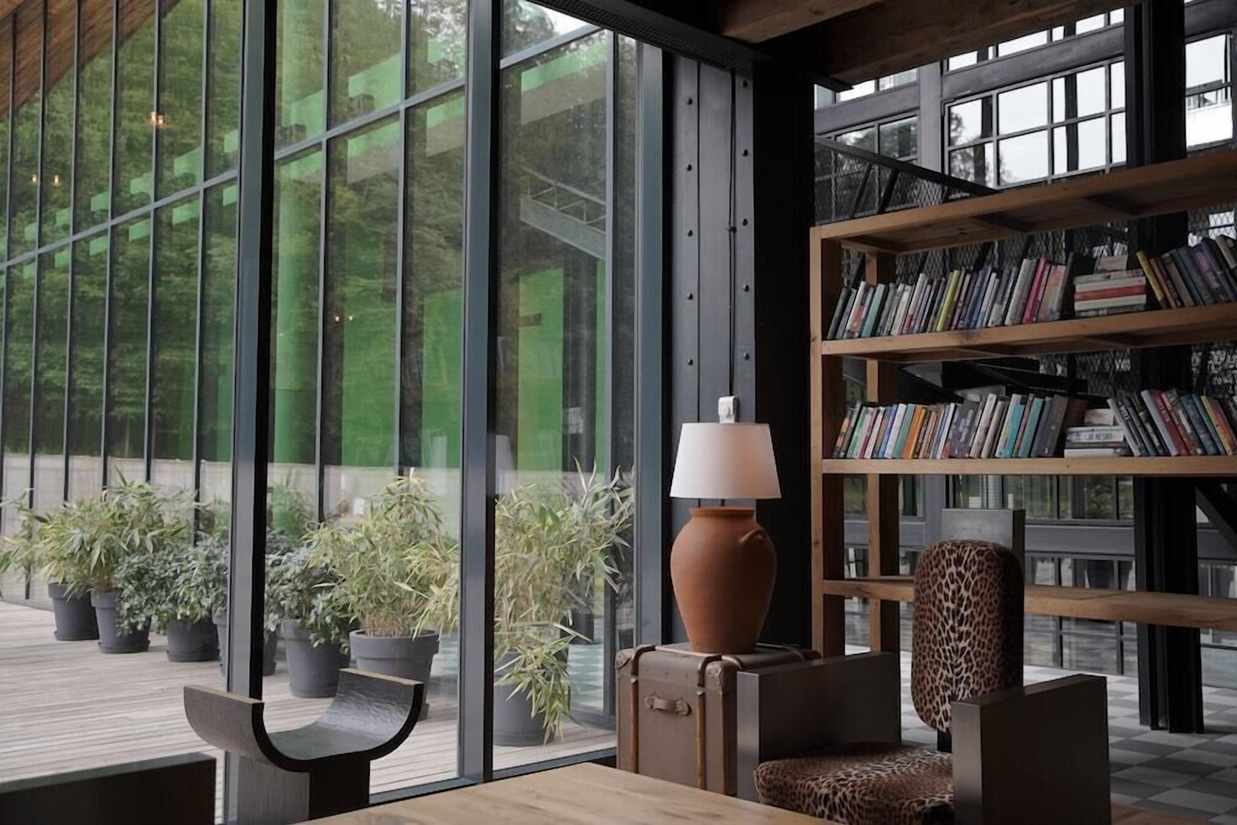 Un interior moderno con ventanas amplias, una estantería, una lámpara y una zona de estar.