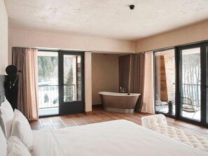 Une chambre à coucher avec un grand lit, une baignoire et un balcon avec des rideaux.
