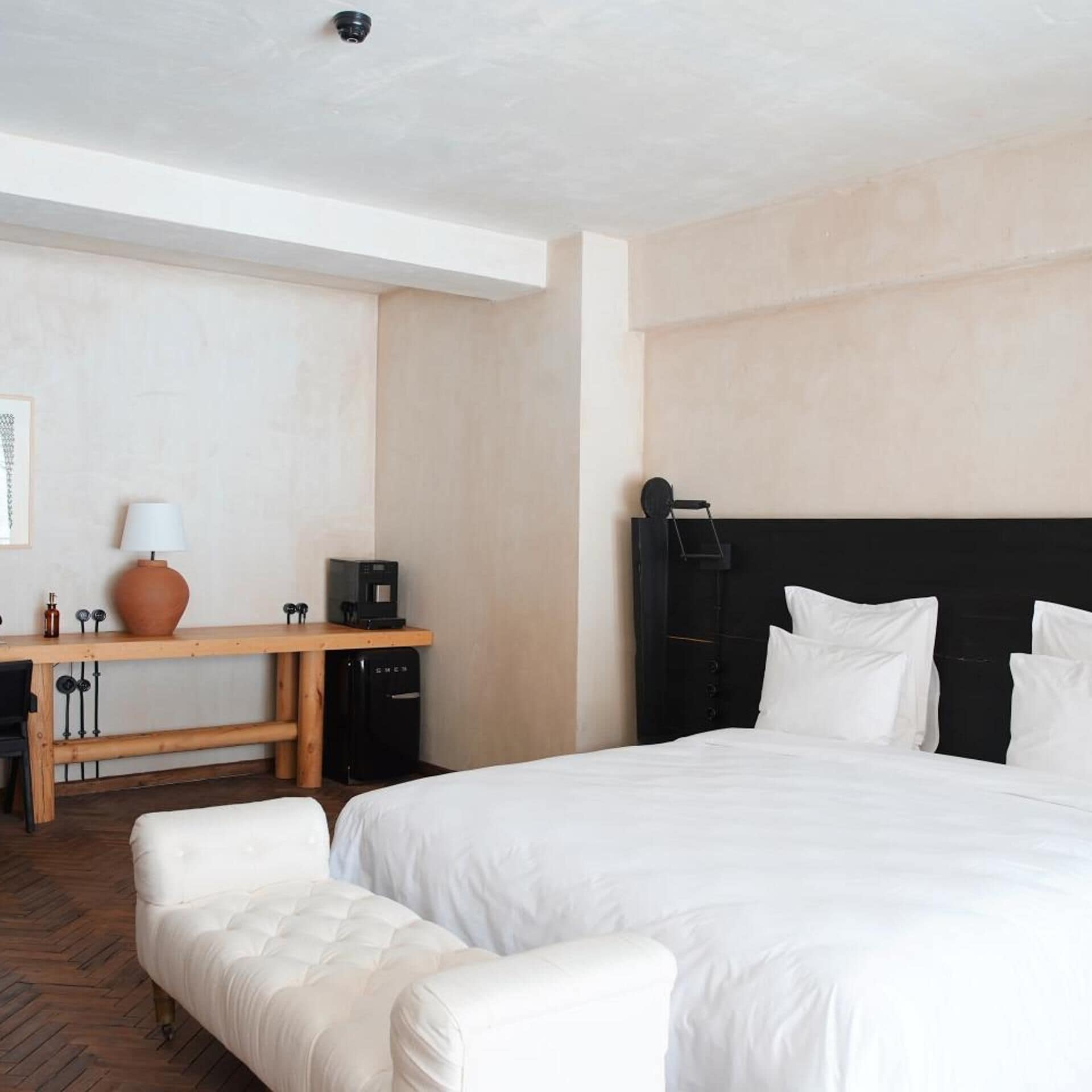 Habitación de hotel con cama, escritorio, silla, refrigerador pequeño y televisor instalado en la pared.