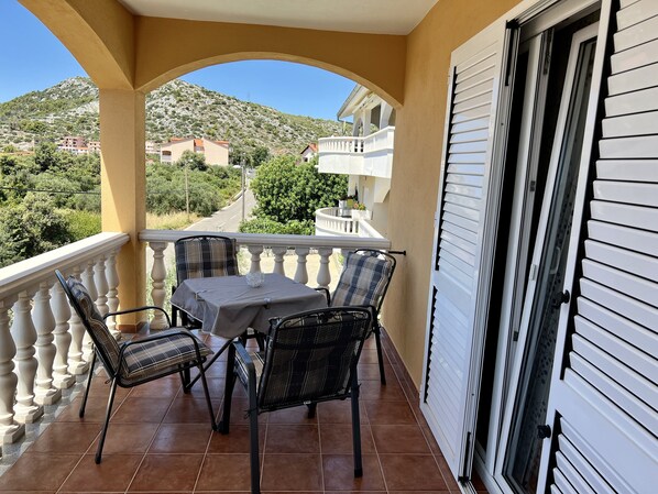 A balcony with a table and chairs, a view of a mountain, and a building in the background.