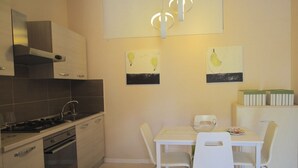 Cocina compacta con estufa a gas, horno y sillas blancas alrededor de una mesa pequeña.