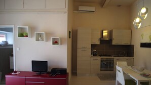 Una cocina compacta con zona de comedor, televisión y un escritorio rojo.