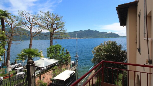 Un balcón con vista a un lago, una montaña a lo lejos y un edificio con baranda roja.