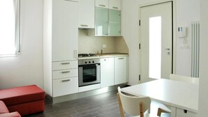 Cozinha moderna com armários brancos, fogão a gás e forno embutido. Há um banco vermelho e uma mesa branca com cadeiras.