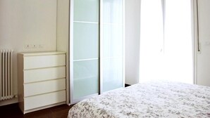 Quarto com cama, guarda-roupa com portas de vidro jateado, radiador e janela.