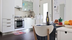 Uma cozinha moderna com armários brancos, forno embutido e área de jantar com mesa posta para dois.