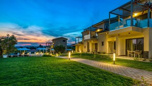 A modern two-story house with a well-maintained lawn, outdoor seating area, and a pathway leading to the entrance. - Miroes Suites (Sithonia)