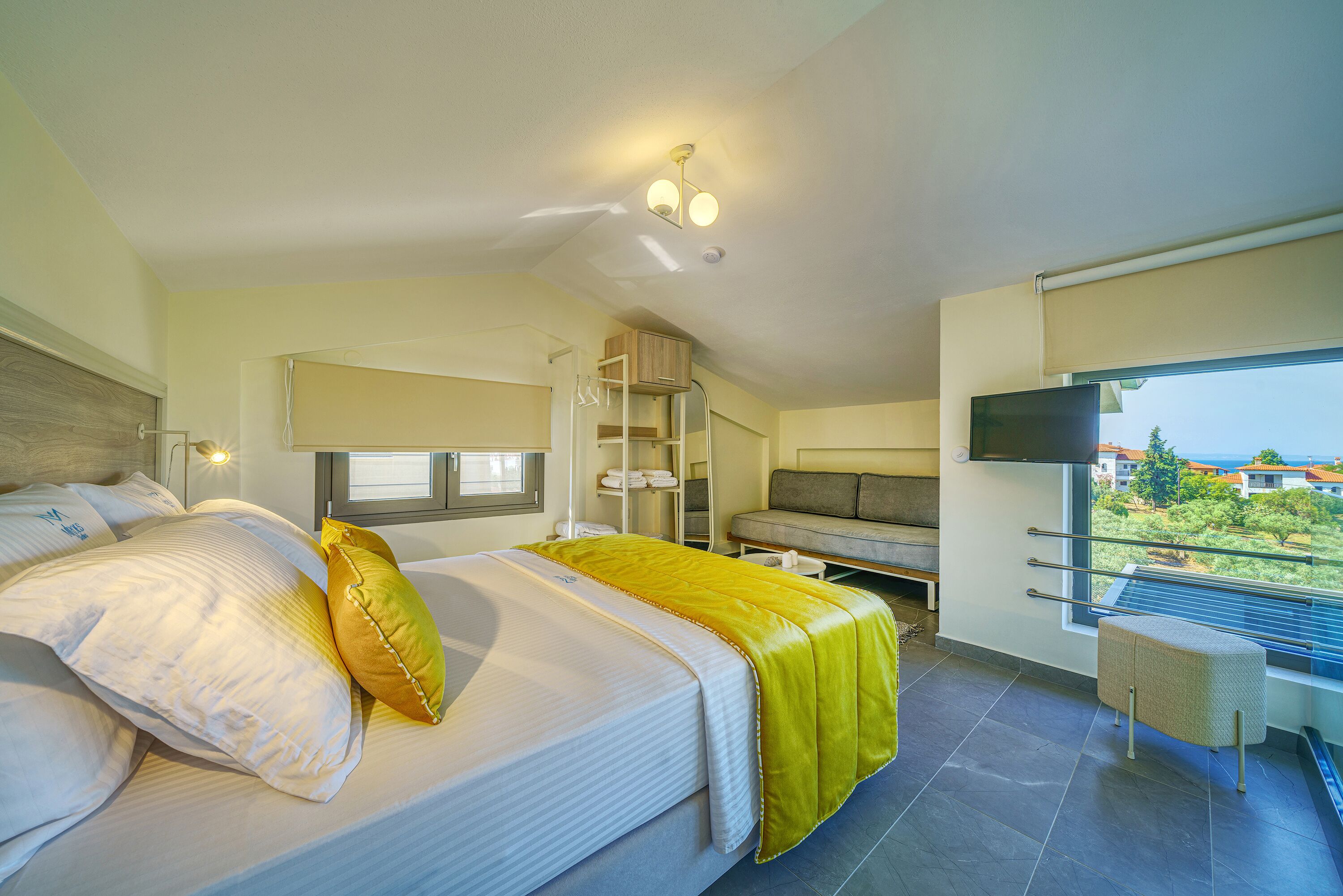 Una habitación de hotel moderna con una cama grande, un sofá, un televisor y un balcón con vistas.